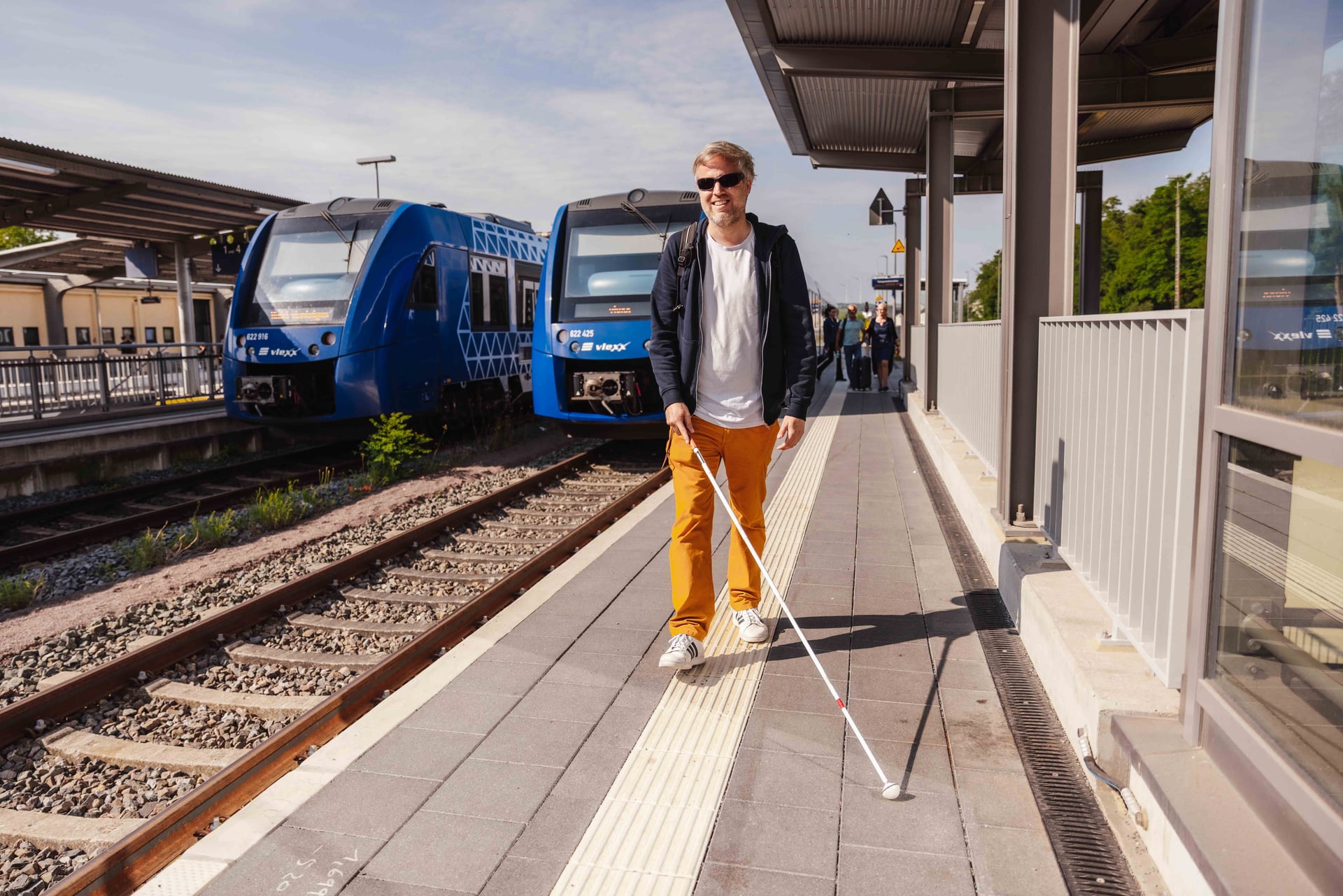 Mann mit Blindenstock läuft am Bahnsteig entlang