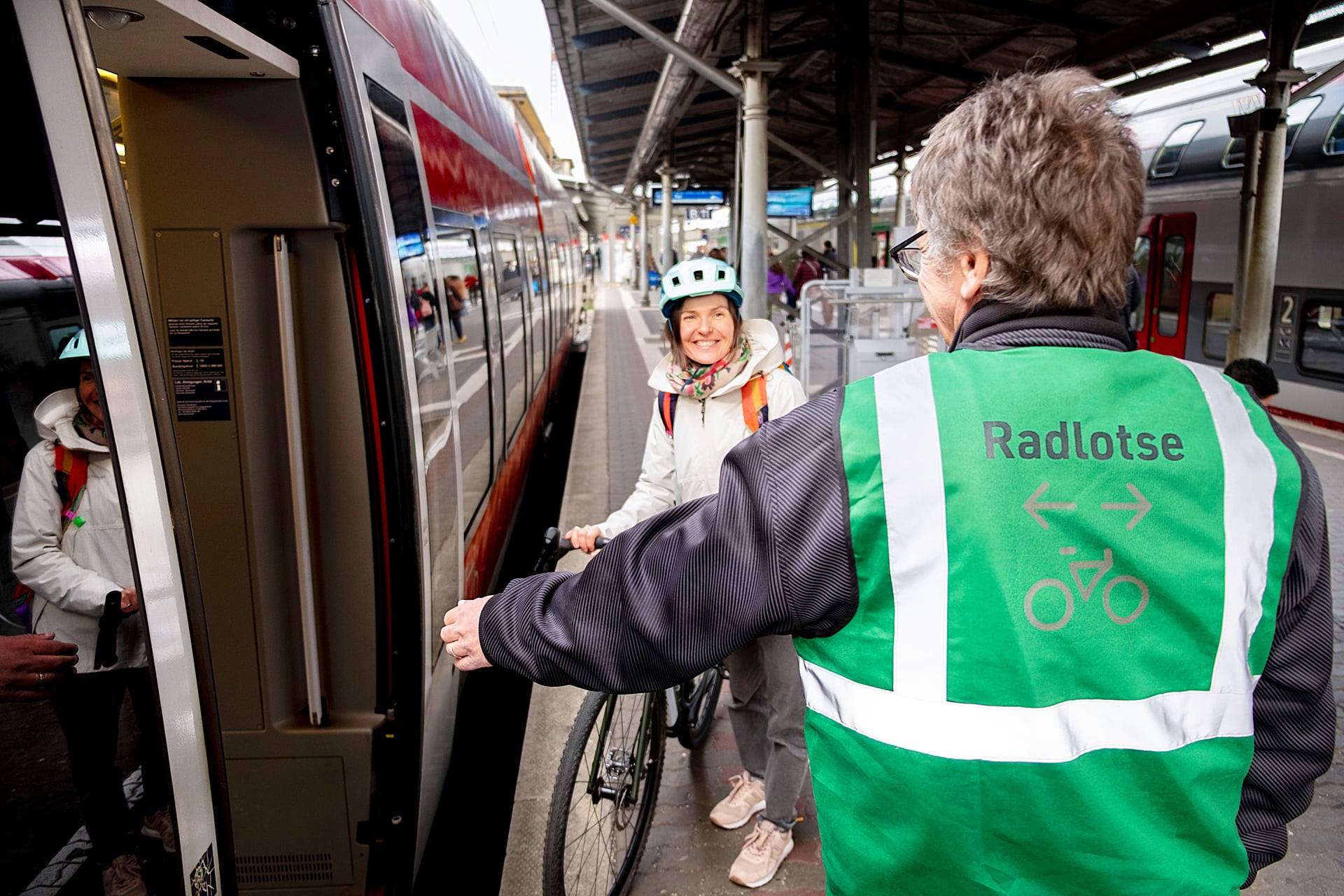 Radlotse unterstützt Frau mit Fahrrad beim Einsteigen in den Zug.